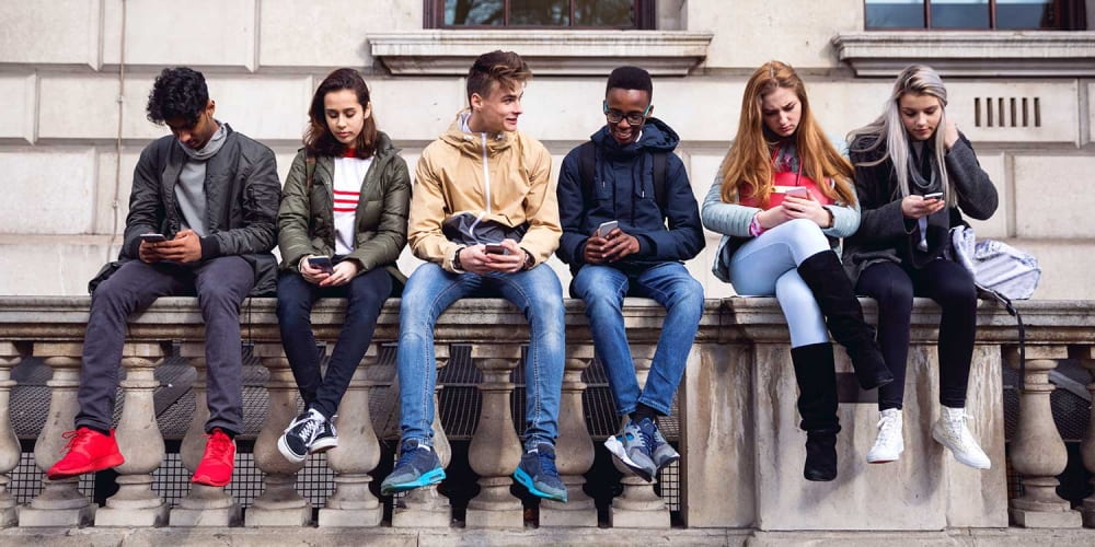 Students sitting outside school on their phones.